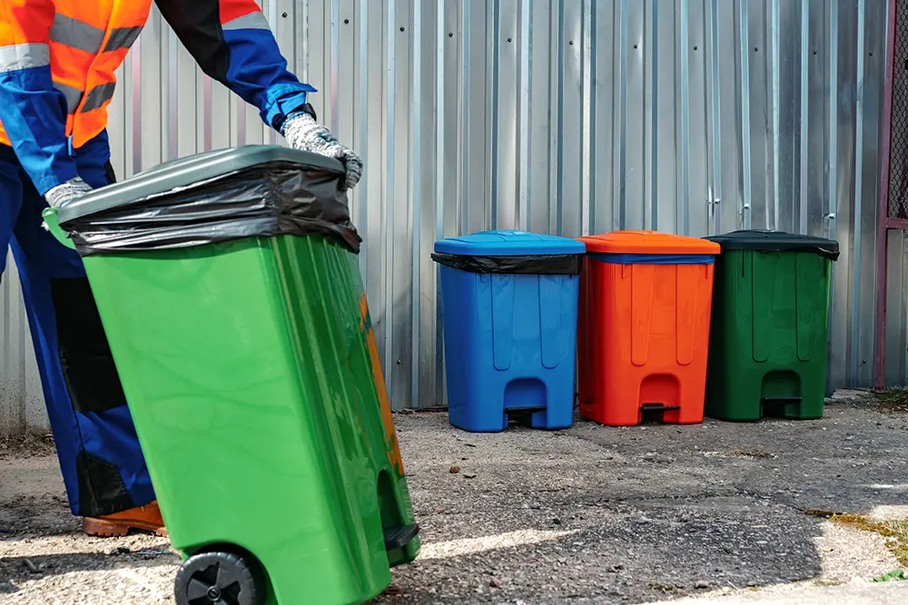 man in safety vest rolling trash can to curb on garbage day resized for web