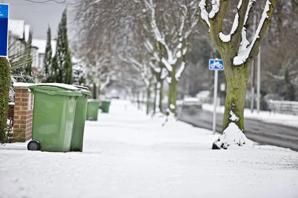 snowy street with trash cans sitting at the curb on grabage day resized for web
