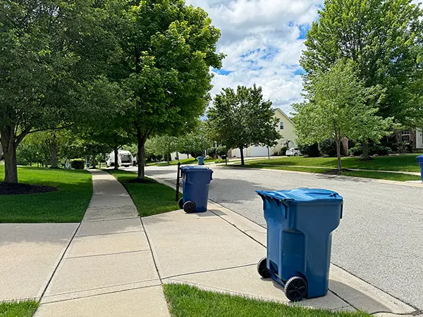 blue trash cans line the street on trash day with a trash truck in the distance